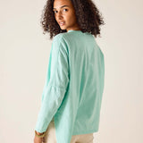 Woman wearing a light green long-sleeve shirt against a beige background