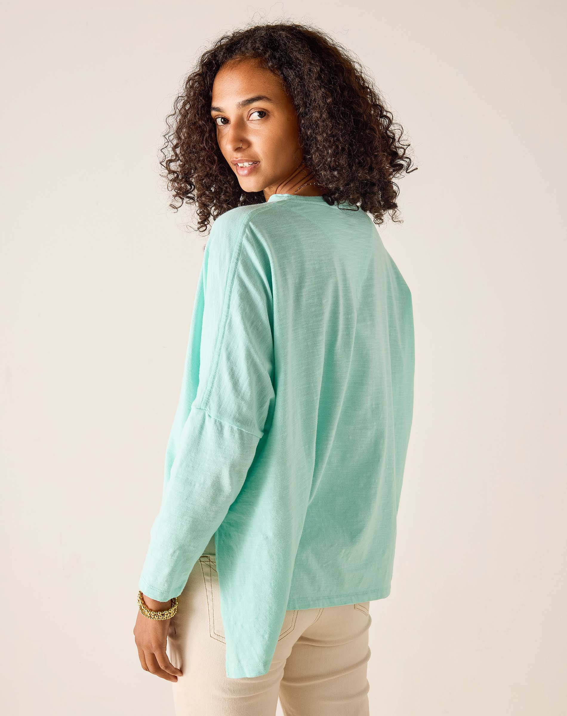 Woman wearing a light green long-sleeve shirt against a beige background