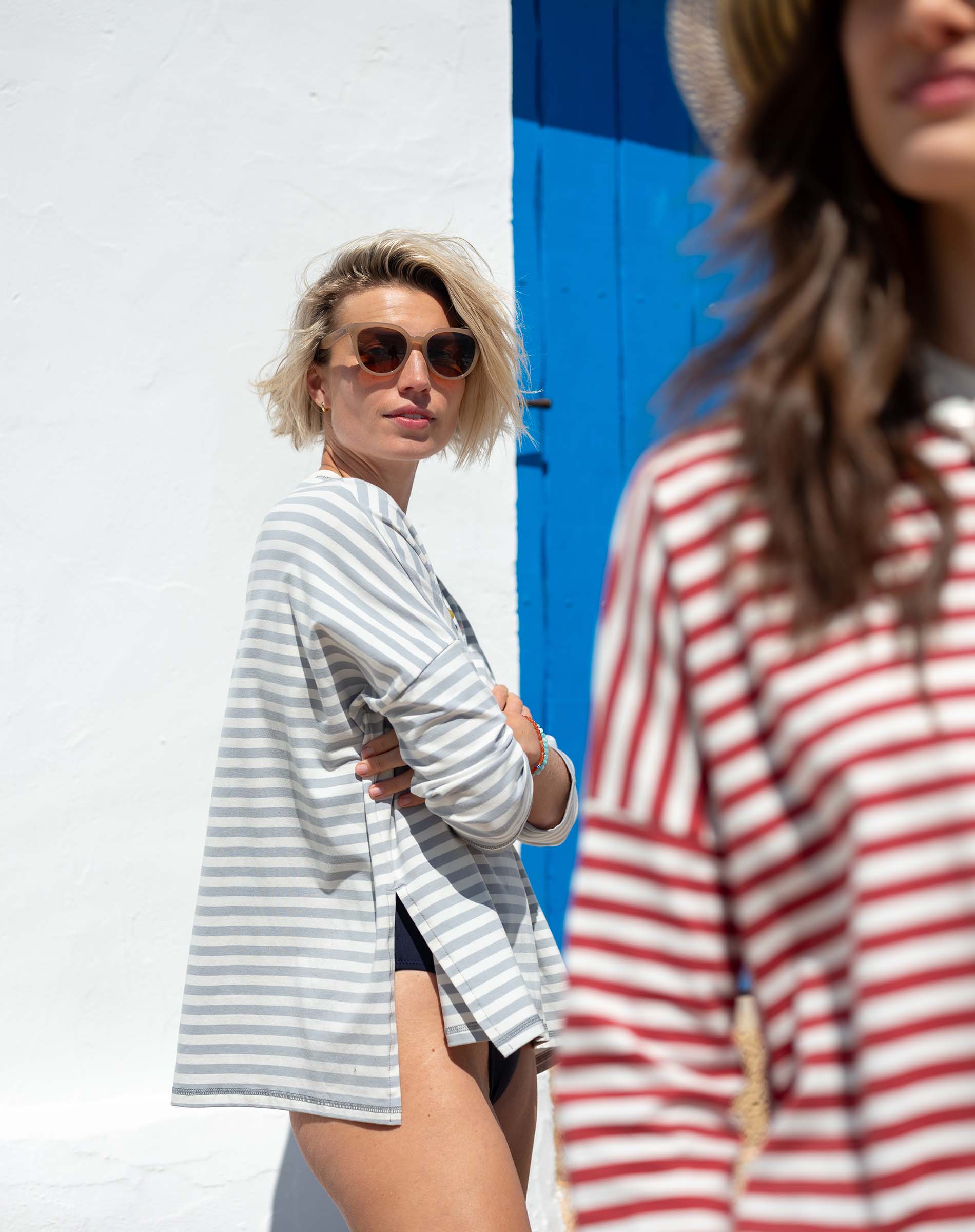 Woman in a striped shirt standing next to a blue door with another person in the foreground.