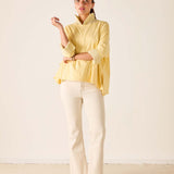 Woman wearing a yellow top and white pants against a plain background