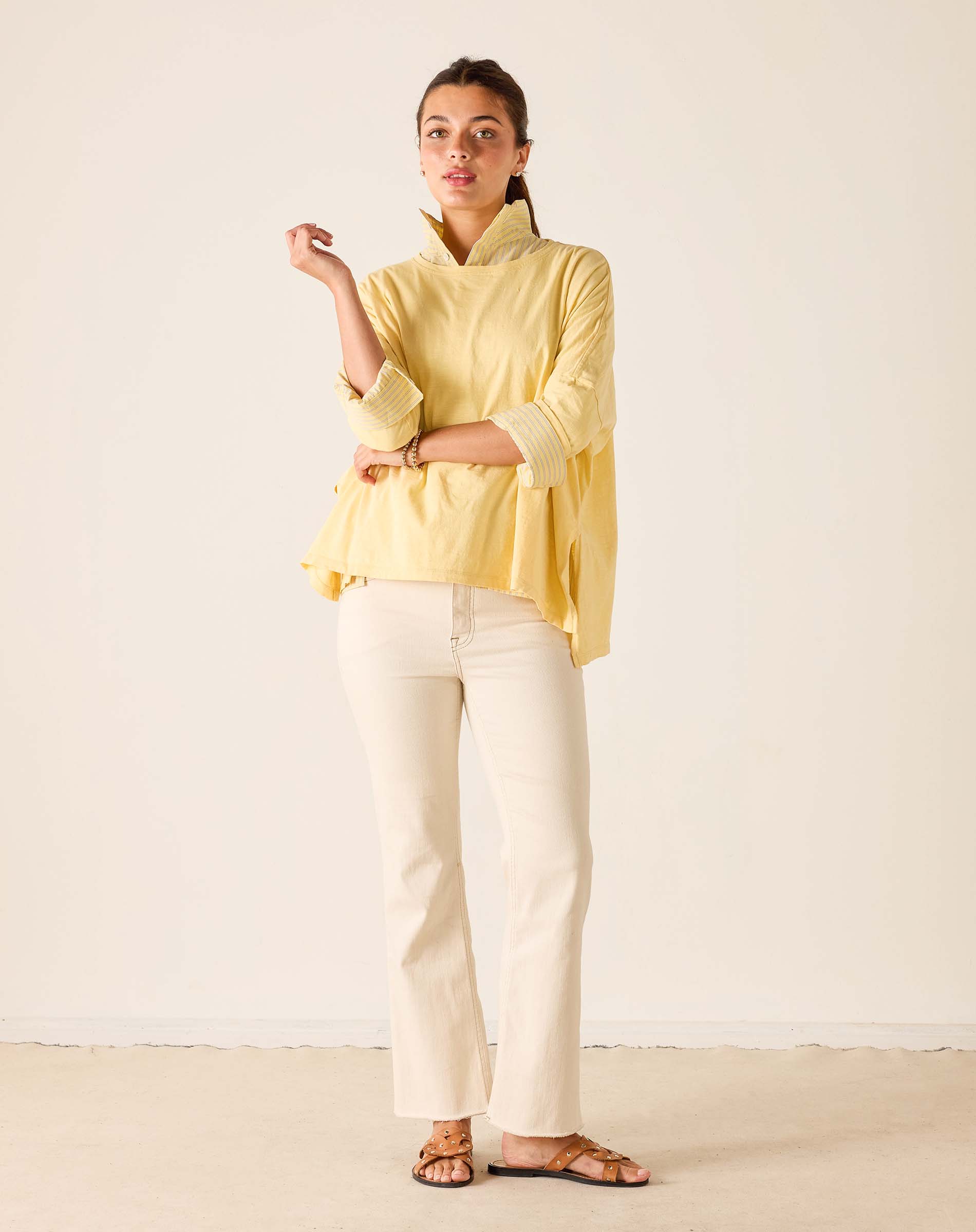 Woman wearing a yellow top and white pants against a plain background