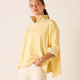 Woman wearing a yellow top with a high collar against a plain background