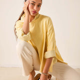 Woman wearing a yellow top and white pants sitting on a beige surface.