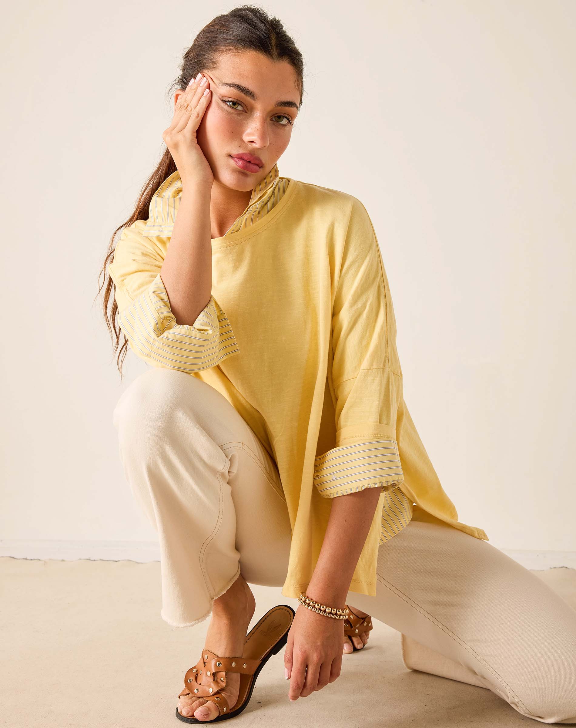 Woman wearing a yellow top and white pants sitting on a beige surface.