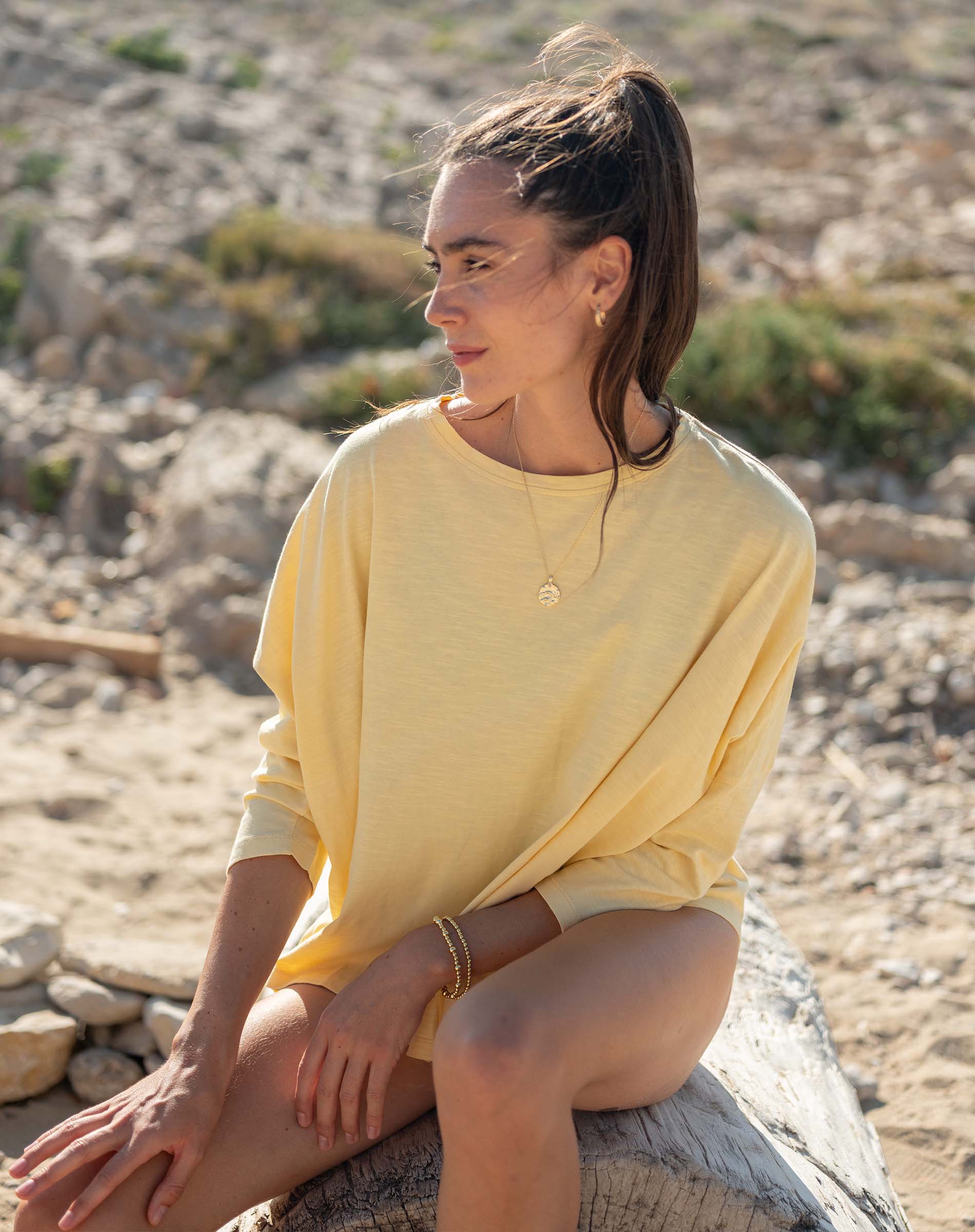 Woman in a yellow dress sitting on a rock with a natural landscape background