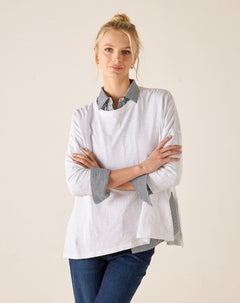 Woman wearing a white shirt with gray accents and blue jeans on a beige background