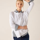 Woman wearing a light gray long-sleeve shirt with rolled-up sleeves and blue jeans on a beige background