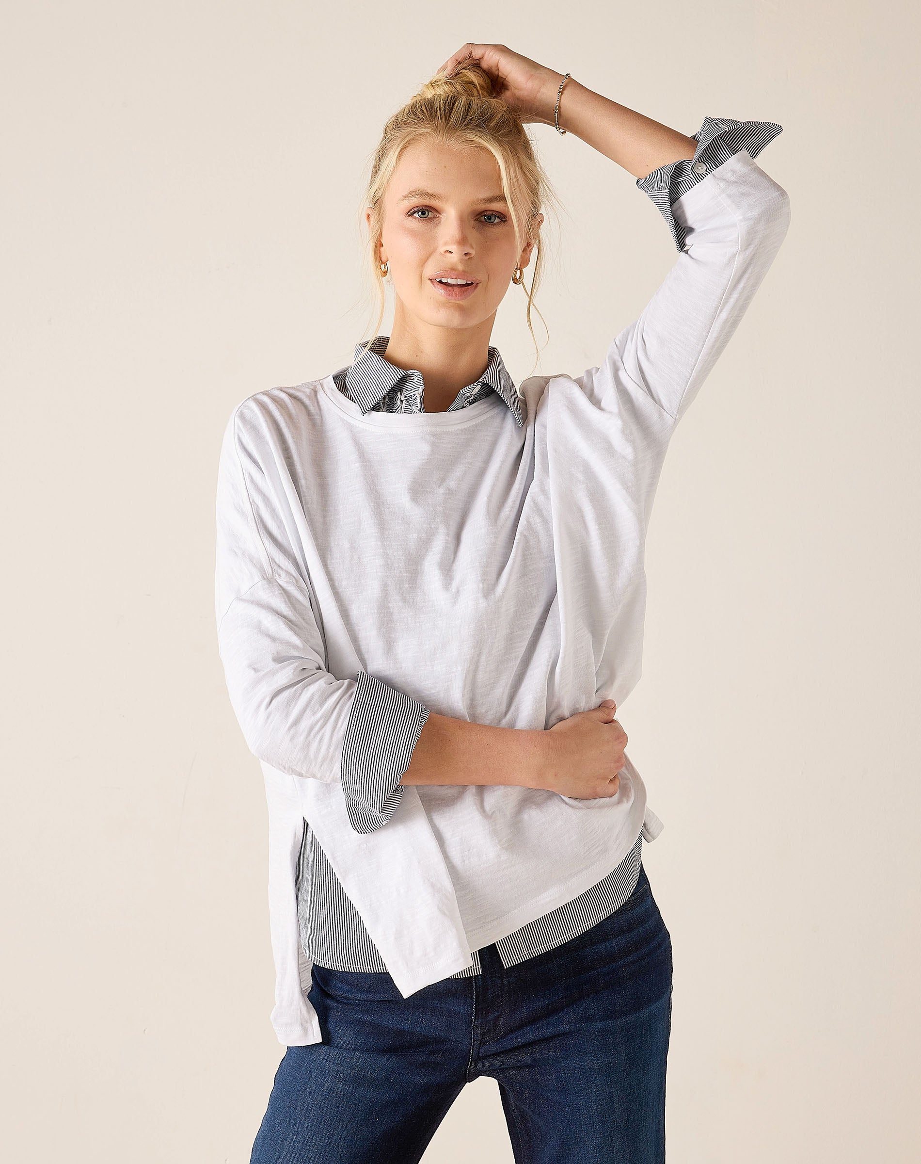 Woman wearing a light gray long-sleeve shirt with rolled-up sleeves and blue jeans on a beige background