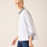 Woman wearing a white shirt with a blue collar and dark jeans on a plain background