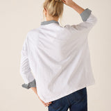 Person wearing a white shirt with rolled-up sleeves and blue pants against a beige background
