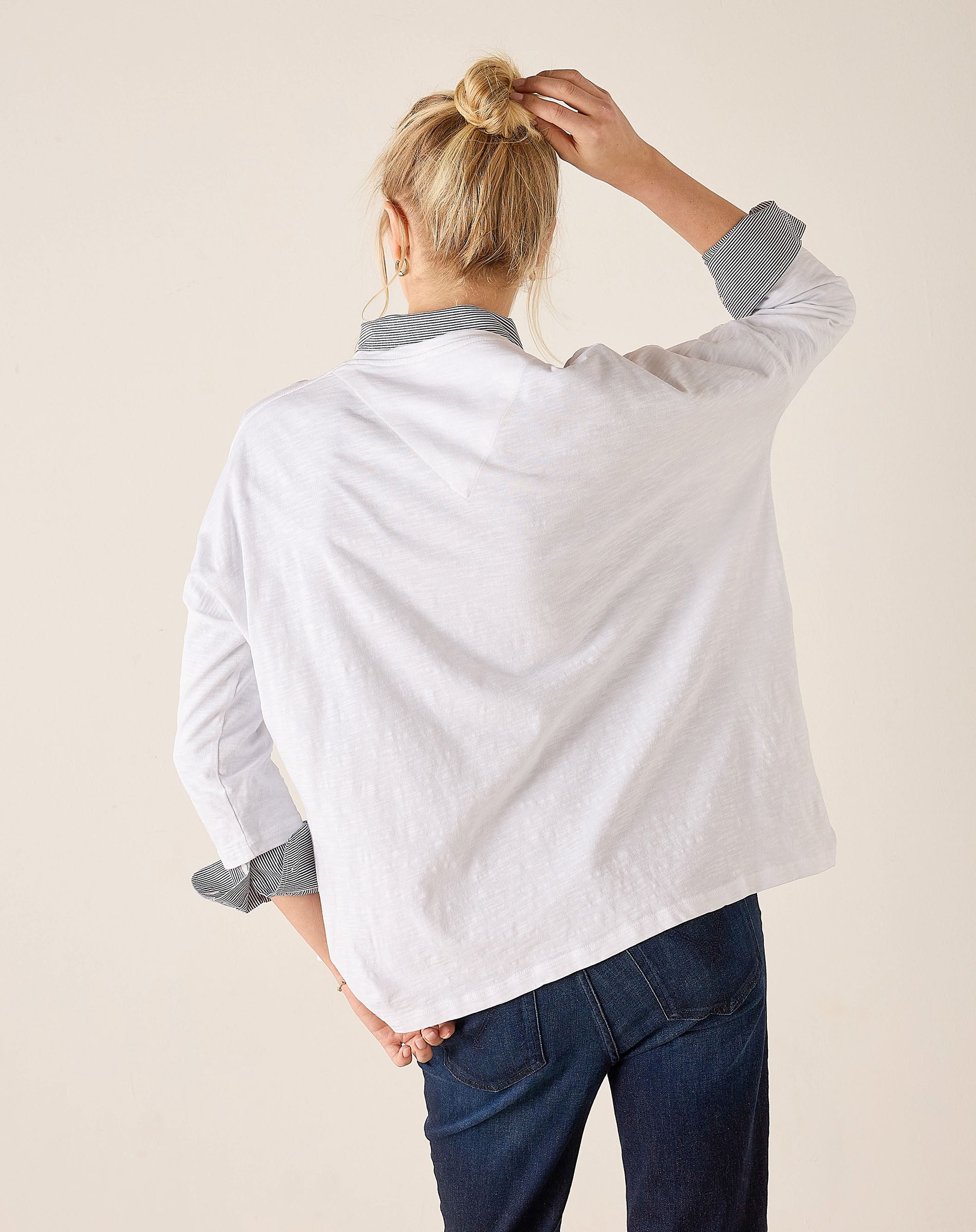 Person wearing a white shirt with rolled-up sleeves and blue pants against a beige background