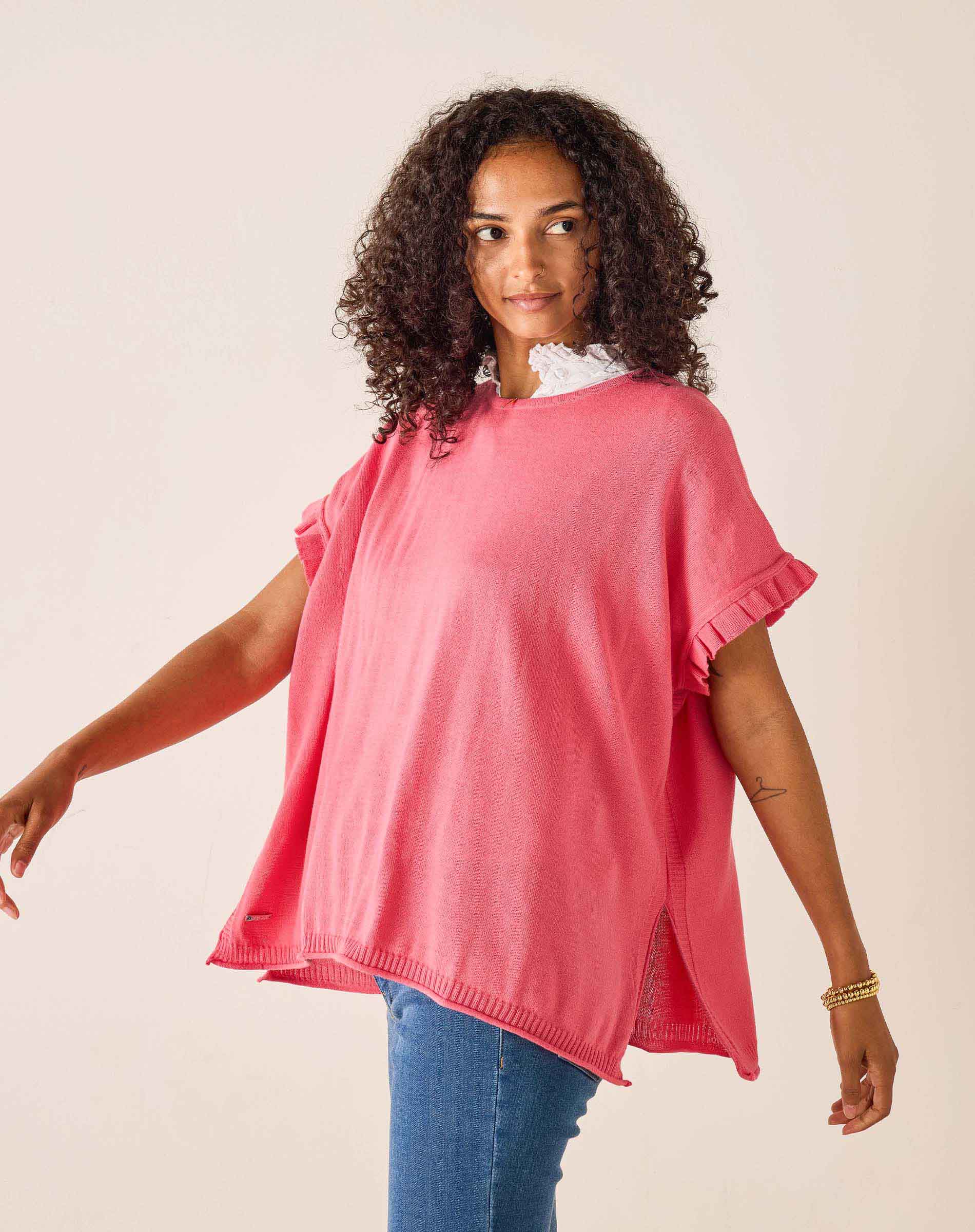 Woman wearing a pink sweater and blue jeans against a plain background
