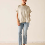 Woman wearing a beige top and light blue jeans against a plain background