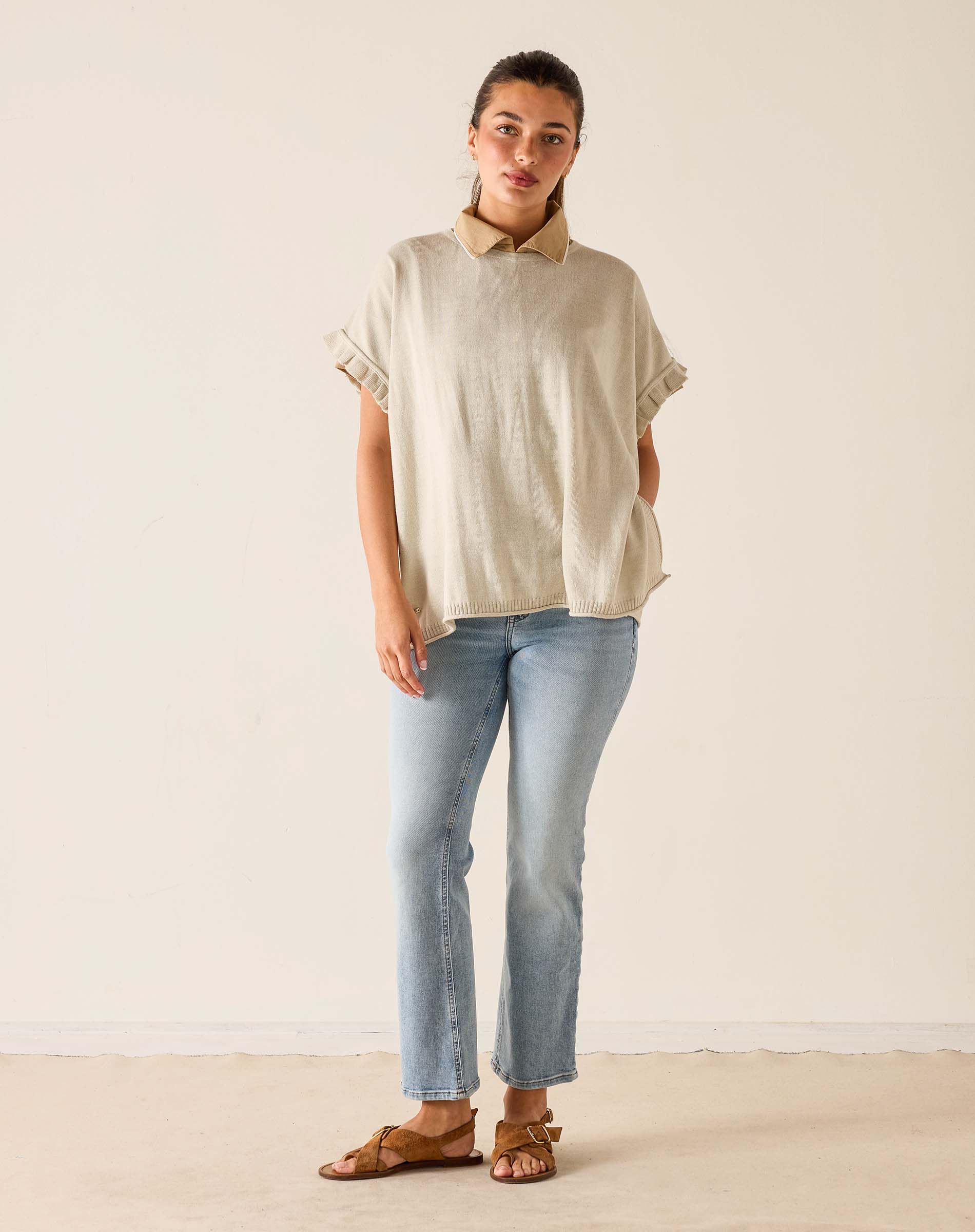 Woman wearing a beige top and light blue jeans against a plain background
