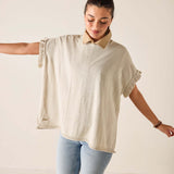 Woman wearing a beige short-sleeve top and light blue jeans against a plain background