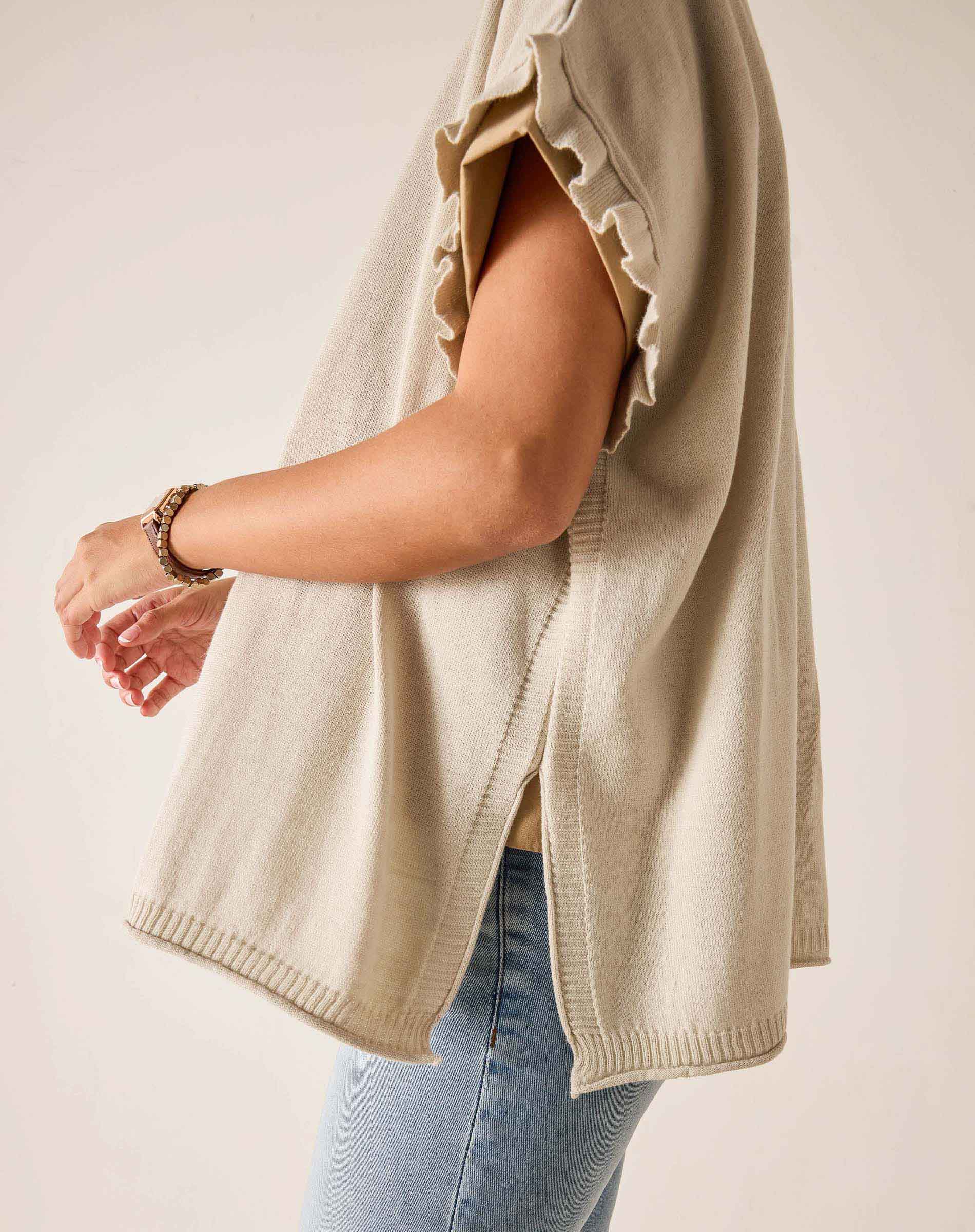 Person wearing a beige sweater and light blue jeans on a plain background