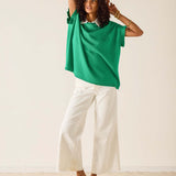 Woman wearing a green top and white pants against a plain background