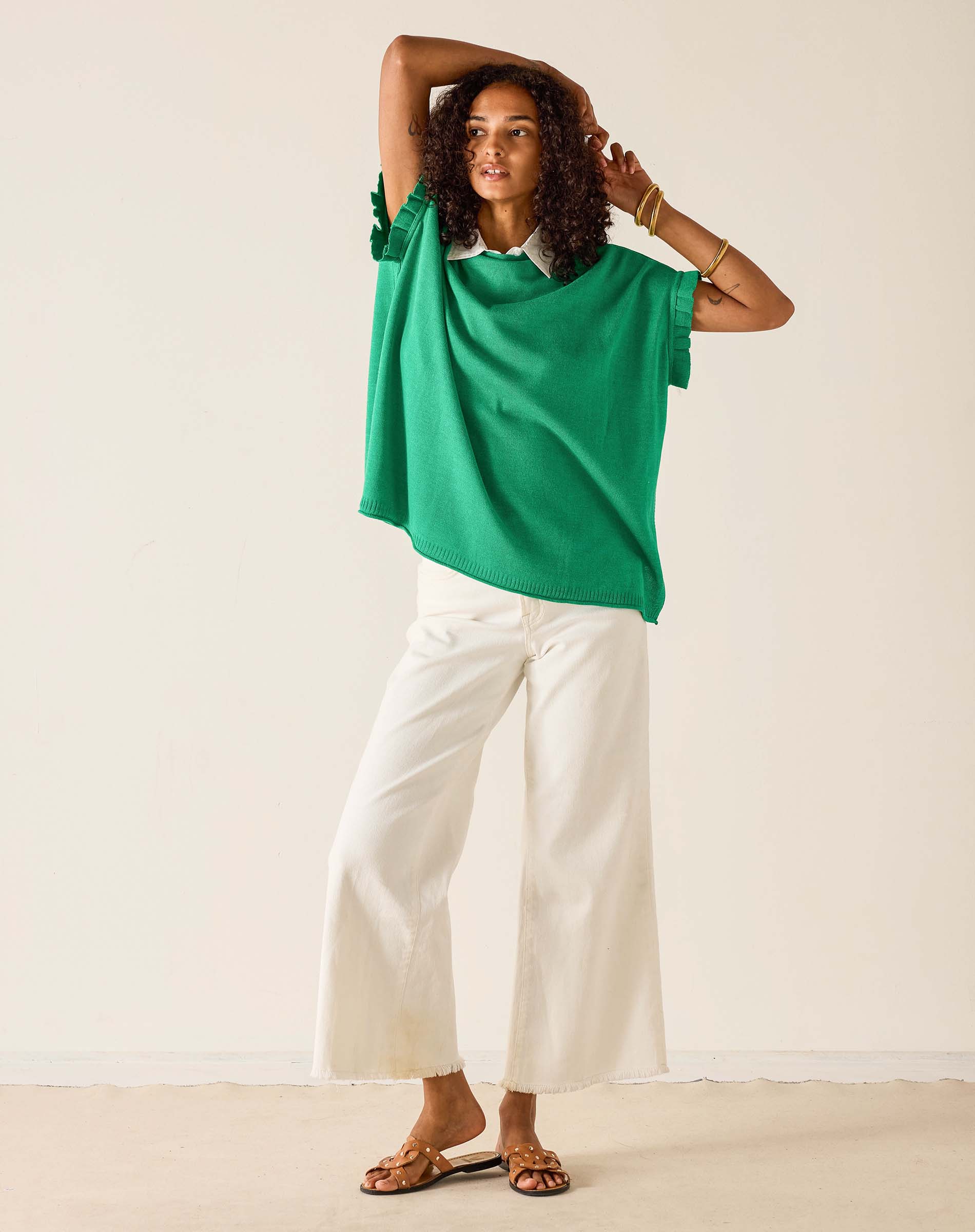 Woman wearing a green top and white pants against a plain background