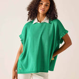 Woman wearing a green sweater over a white shirt on a plain background