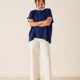 Woman wearing a blue top and white pants standing against a plain background