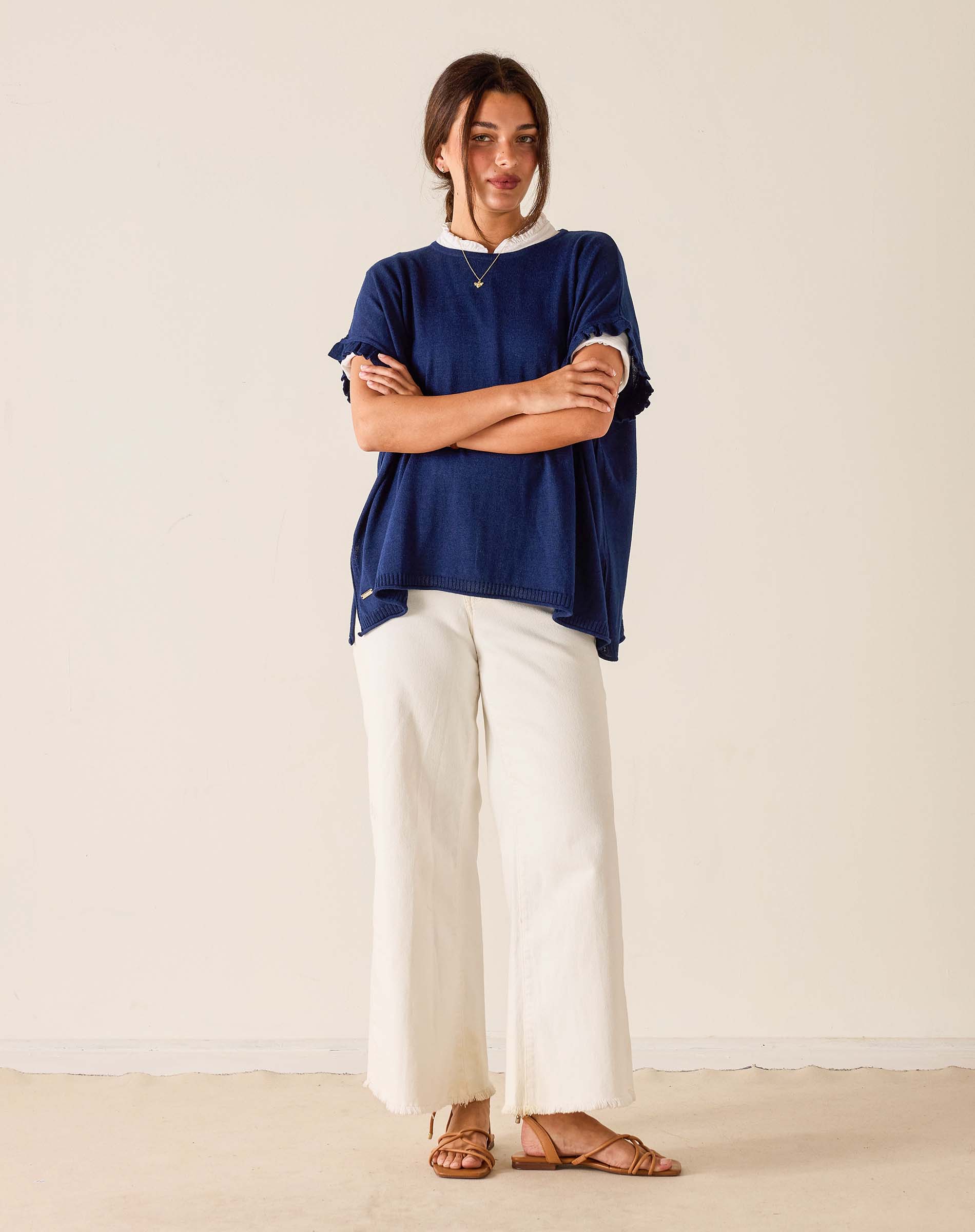 Woman wearing a blue top and white pants standing against a plain background