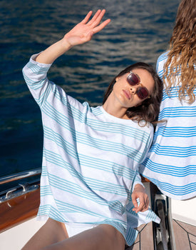 female wearing white long sleeve tee shirt with blue stripes laying on a boat looking at the sun