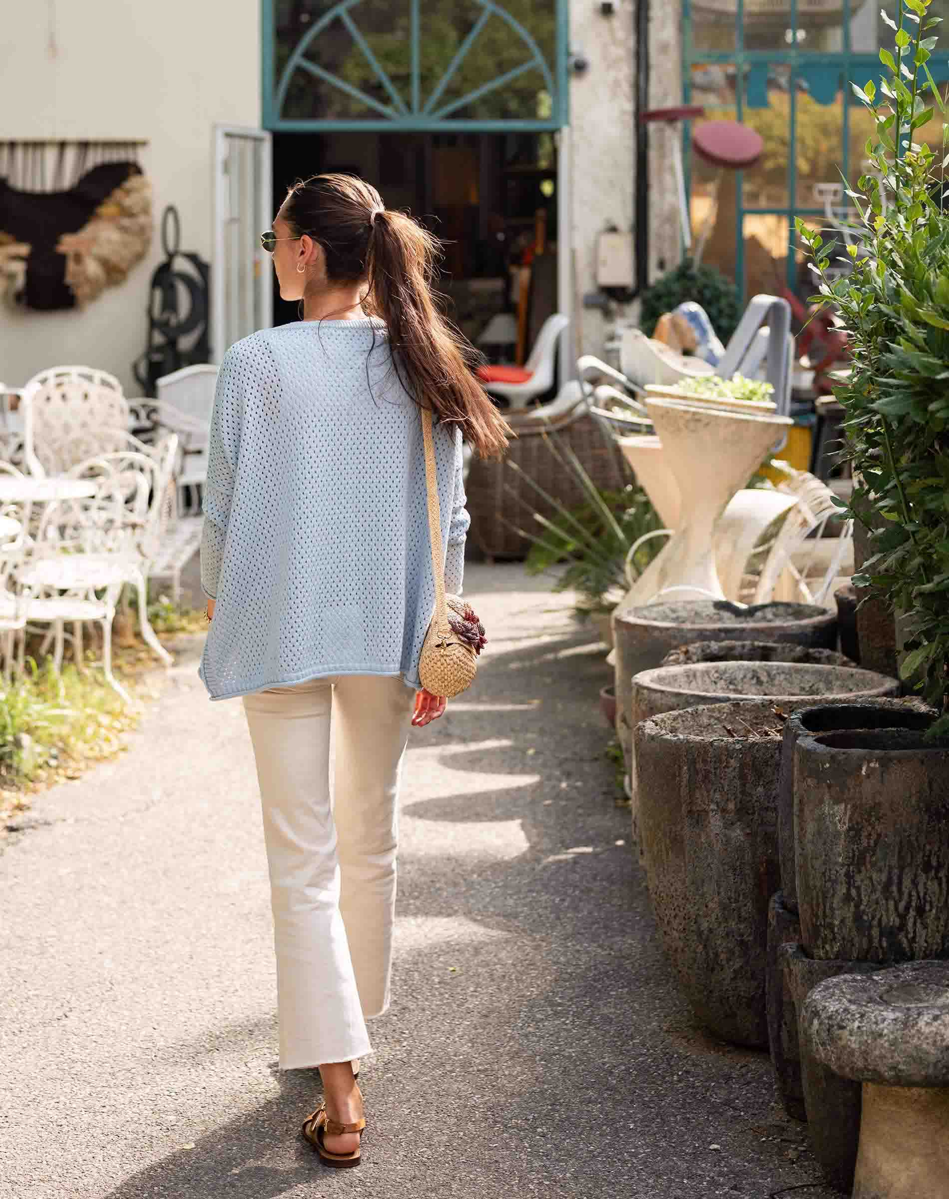Woman walking along a sidewalk with outdoor furniture and plants in the background