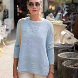Woman wearing a light blue sweater and sunglasses outdoors.