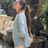 Woman in a light blue sweater and beige pants standing among potted plants.