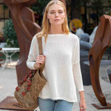 Woman in a white sweater holding a woven bag outdoors