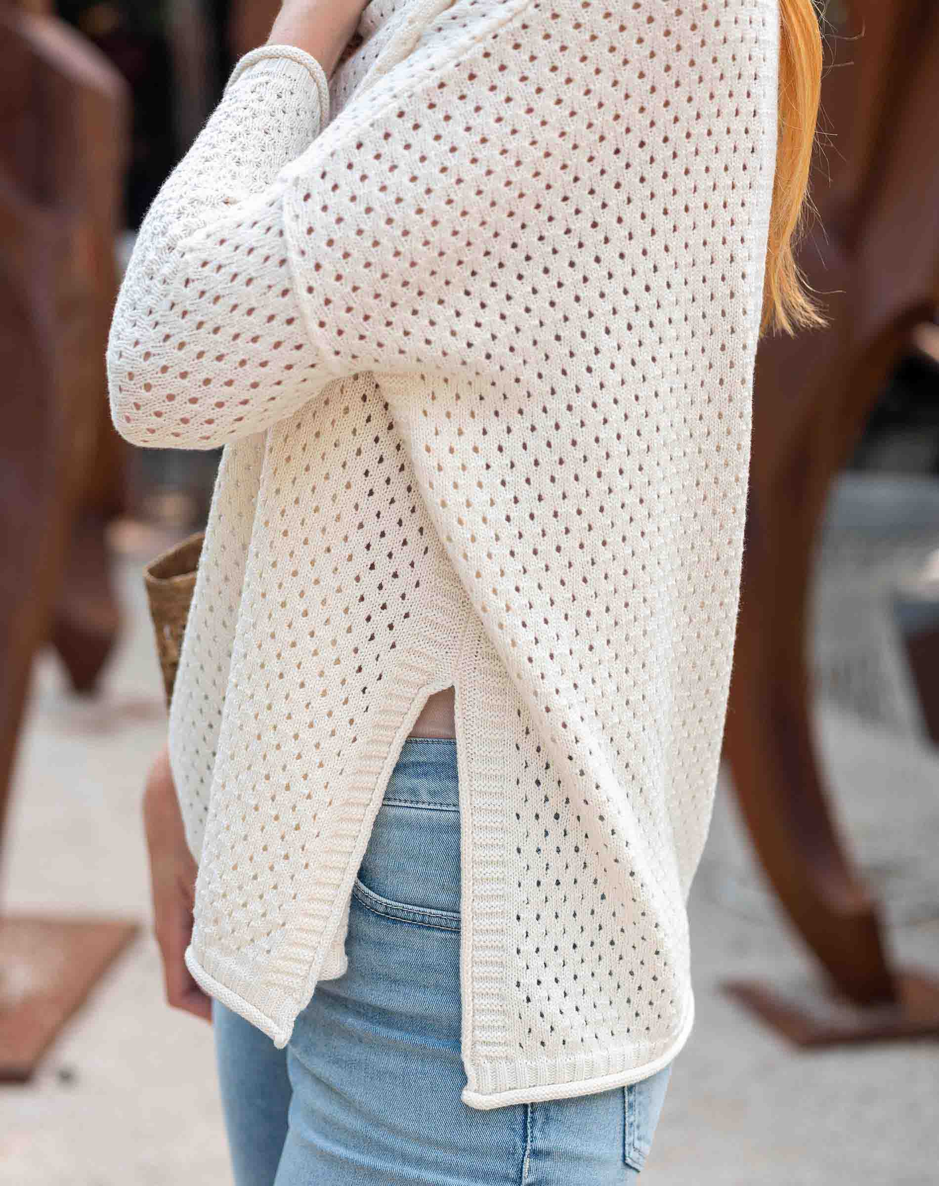 Person wearing a white textured sweater and blue jeans in an indoor setting