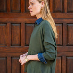 Woman wearing a green sweater and blue shirt against a wooden door background