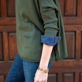 Person wearing a green sweater with rolled-up sleeves and blue jeans, standing against a wooden door.