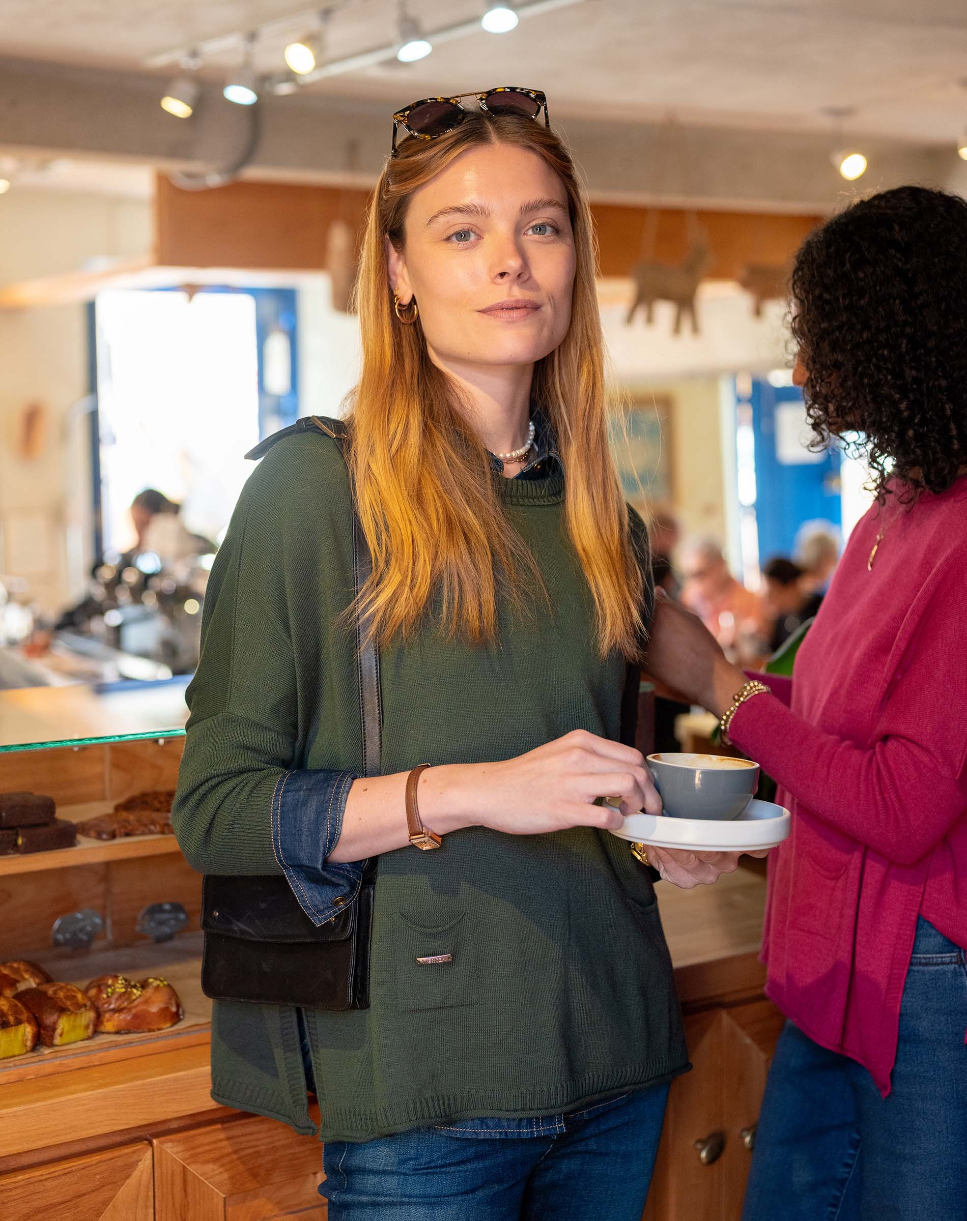 Two women in a store, one holding a coffee cup, with a blurred background