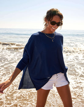 female wearing navy sweater with split sides and white shorts walking in the water on the beach