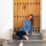 female wearing deep blue sweater with split sides sitting on steps in front of a brown door