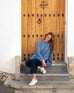 female wearing deep blue sweater with split sides sitting on steps in front of a brown door