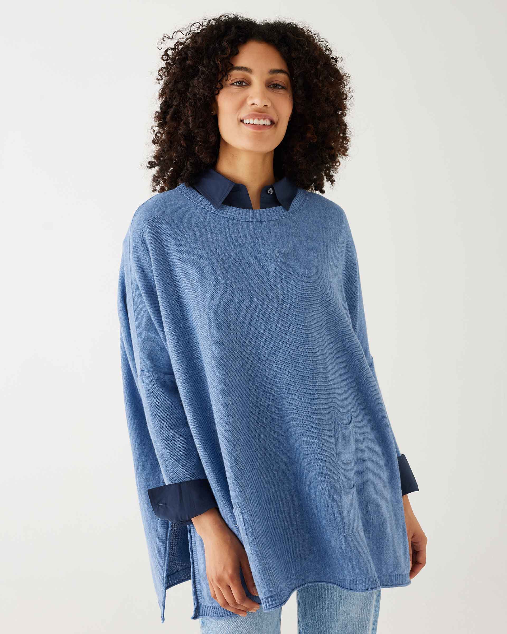 female wearing deep blue sweater with blue shirt cuffed with split sides on a white background