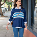 Woman wearing a blue sweater with white stripes and blue jeans, standing on a sidewalk.
