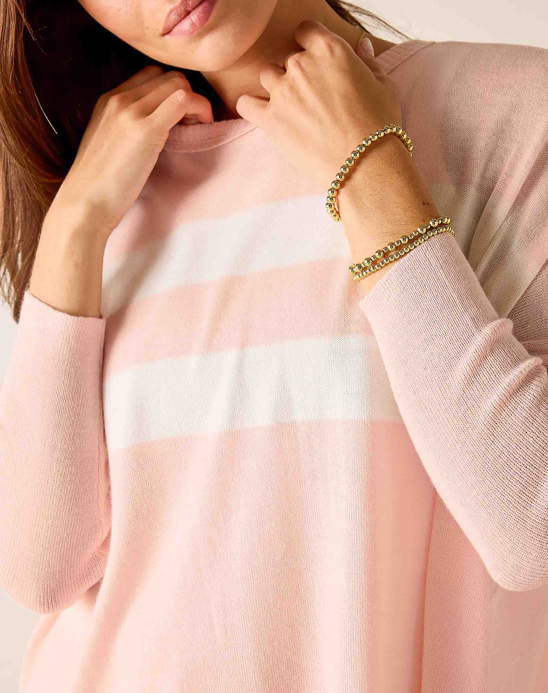 Close-up of a person wearing a pink sweater with a white stripe, holding their collar.