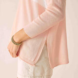 Person wearing a light pink cardigan over a white top with a neutral background