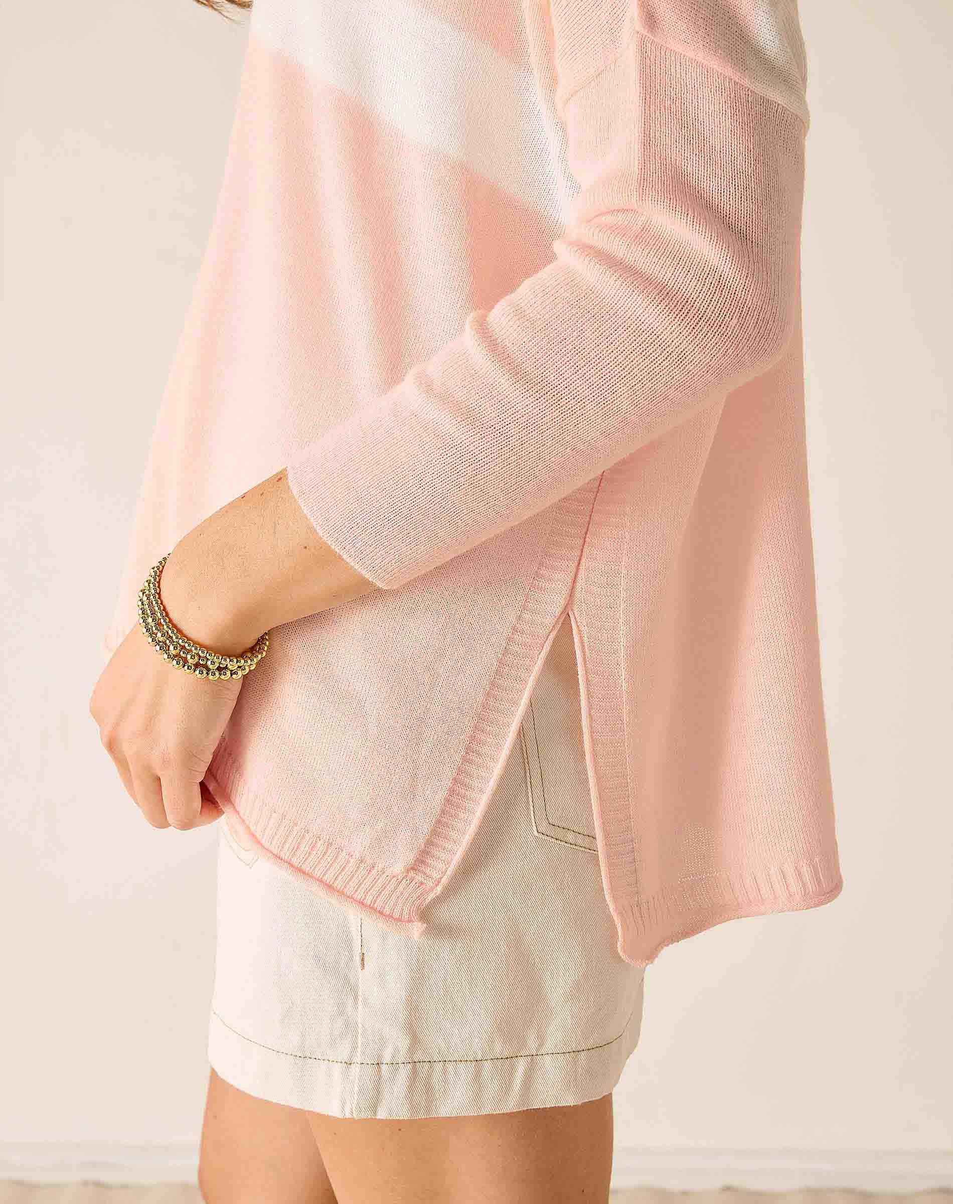 Person wearing a light pink cardigan over a white top with a neutral background