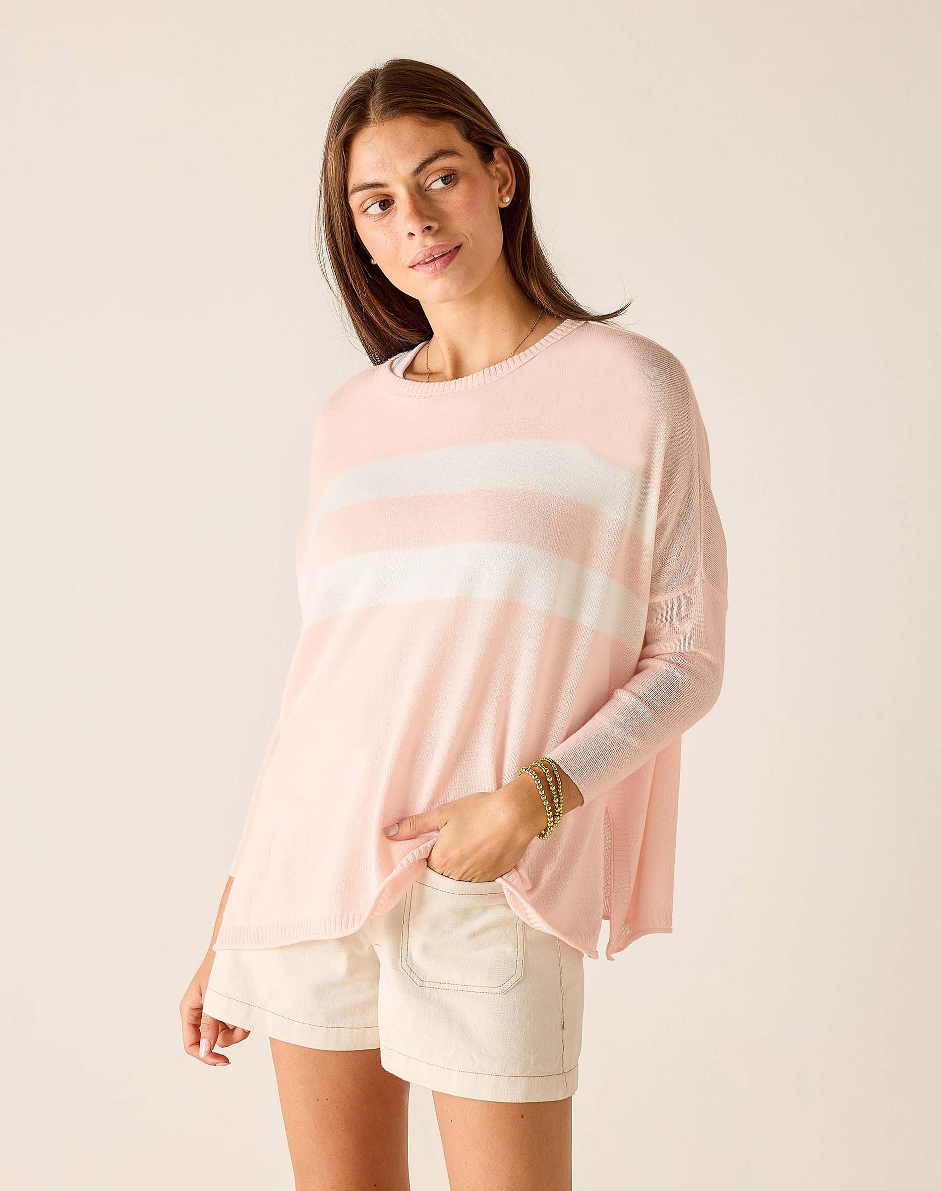 Woman wearing a light pink long-sleeve top with a white stripe and white shorts on a beige background