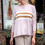 Woman wearing a light pink sweater with brown and white stripes, beige pants, and a beige cap outdoors.