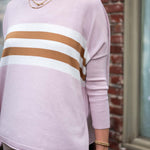 Person wearing a light pink sweater with brown and white stripes, standing against a brick wall.