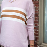 Person wearing a light pink sweater with brown and white stripes, standing against a brick wall.