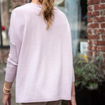 Person wearing a light pink long-sleeve top and beige pants in an urban setting.