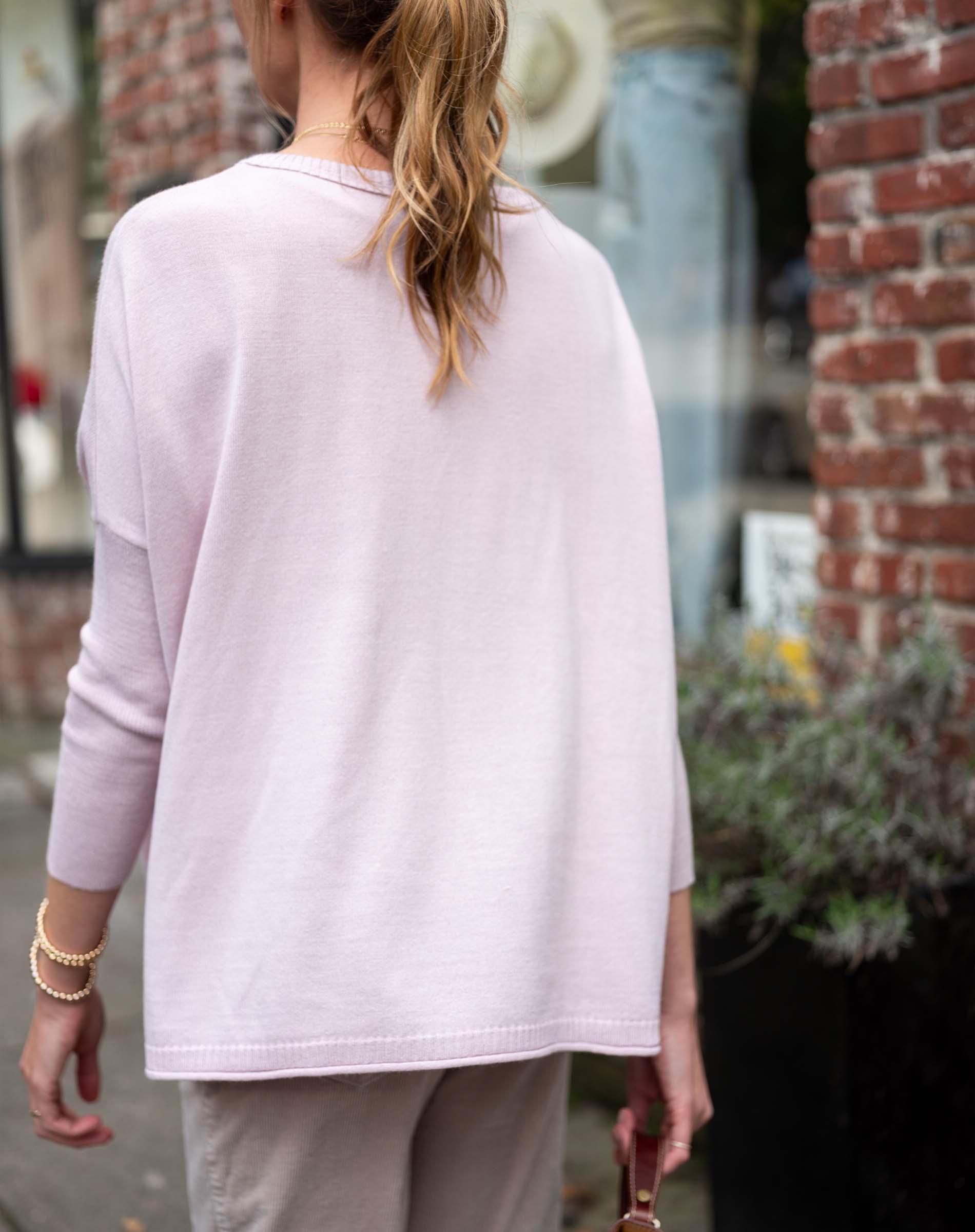 Person wearing a light pink long-sleeve top and beige pants in an urban setting.