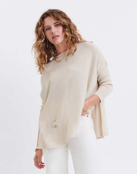 female wearing sand sweater with split sides and white jeans on a white background