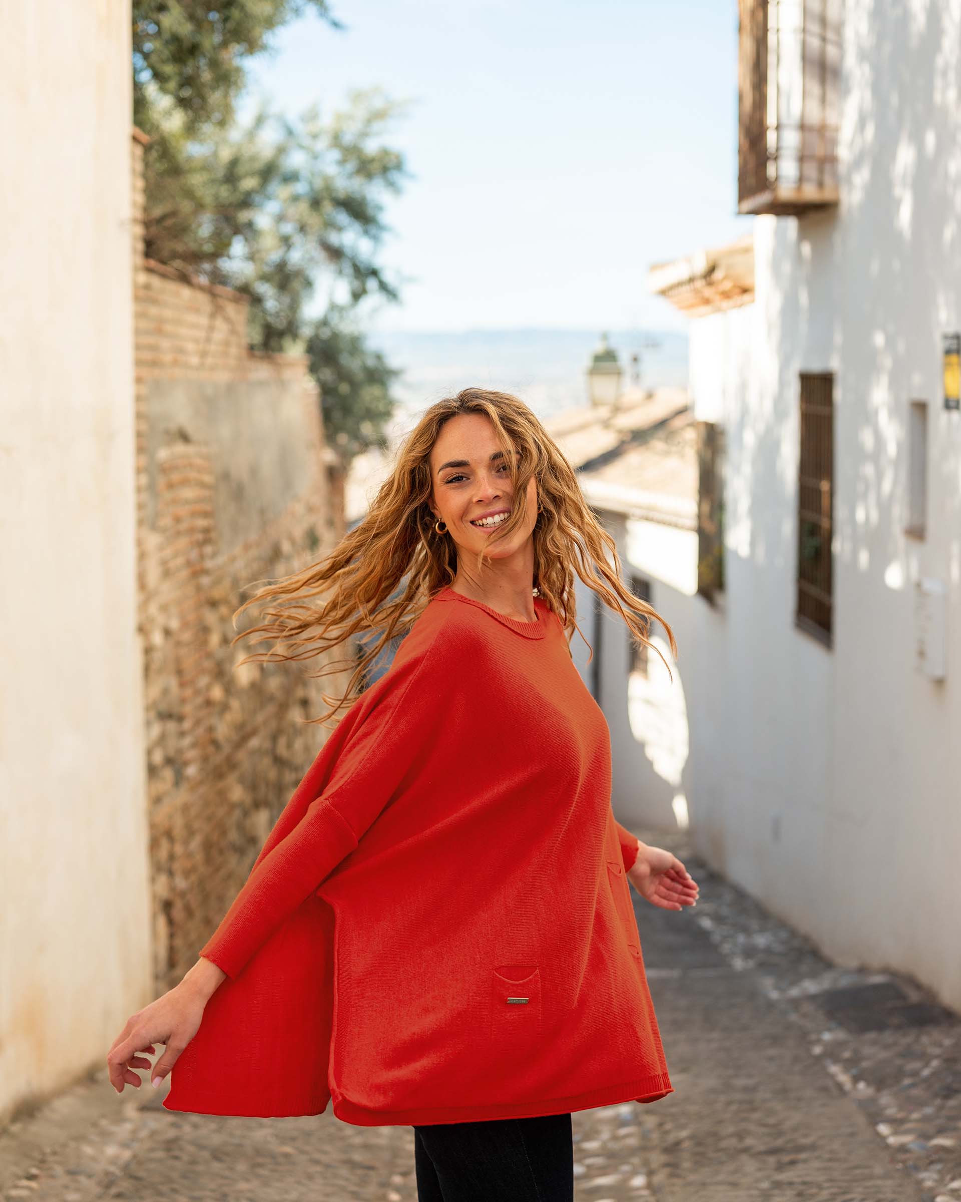 female wearing red sweater with dark jeans spinning in the streets of the country side of spain